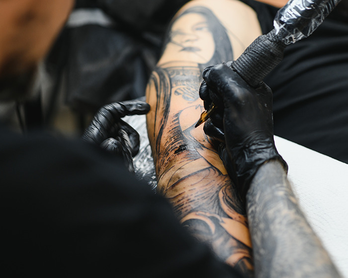 Artista de tatuajes con guantes negros creando una manga detallada del tatuaje en el brazo del cliente en un entorno de estudio profesional.