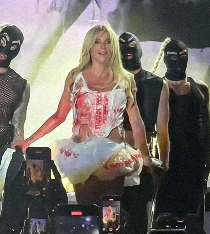 Kesha actuando en Mighty Hoopla con bailarines en máscaras, participando en un acto controvertido y provocativo en el escenario.