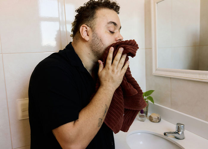Hombre secando la cara con toalla en el baño que simboliza la molestia sobre el novio de la compañera de cuarto usando su ducha.