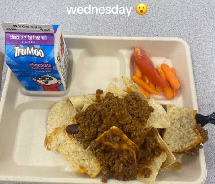 Almuerzos escolares estadounidenses con chile con papas fritas, zanahorias para bebés, rodaja de tomate y cartón de leche con chocolate en la bandeja.