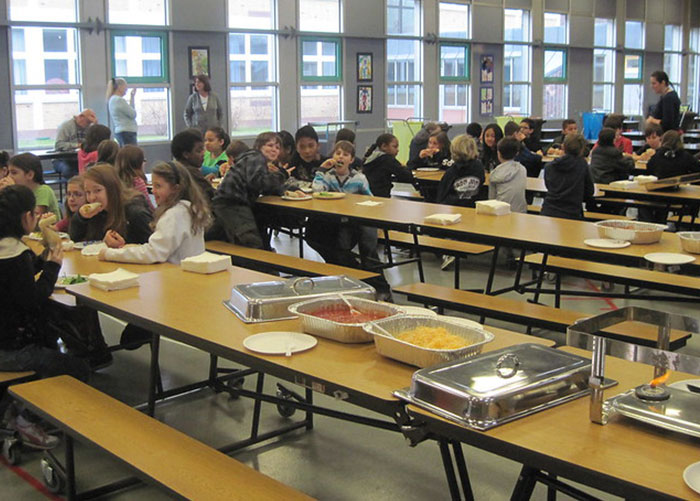 Adolescentes en una cafetería escolar estadounidense almorzando, mostrando almuerzos escolares estadounidenses típicos y ambientes gastronómicos.