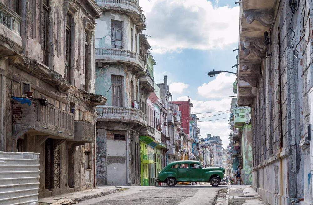 La historia del Cortado: se ve un automóvil verde conduciendo por una colorida calle en Cuba.