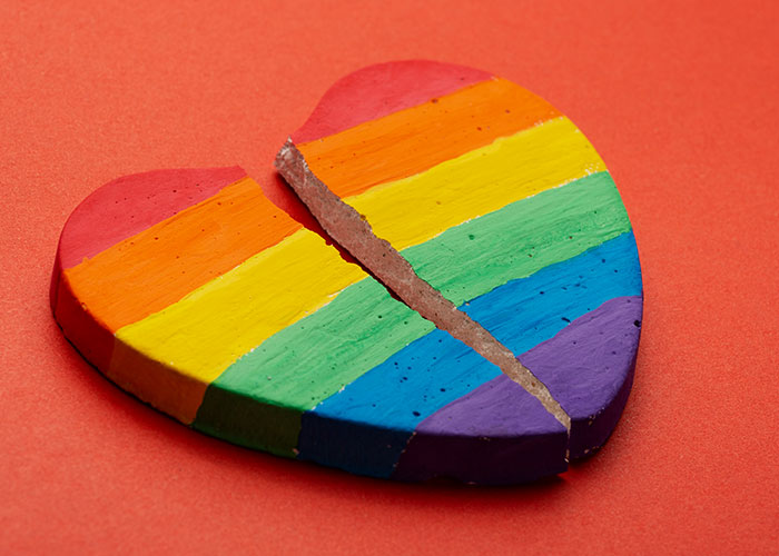 Corazón roto pintado con colores del arco iris sobre fondo rojo, simbolizando a la mujer roma sobre viajar con un conflicto de amigos.