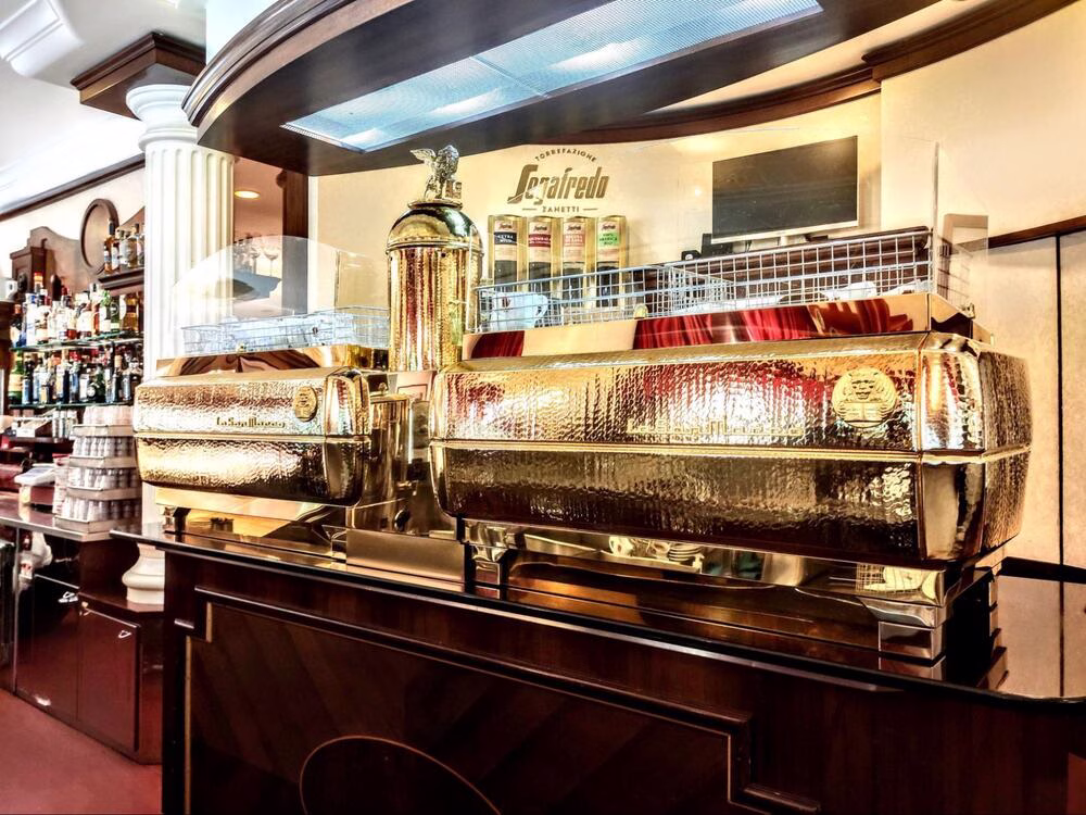 Un café tradicional en Italia. El Cafe Bar, que está hecho de una madera de color oscuro, está cubierto con dos grandes máquinas de café espresso de La Marzocco doradas.