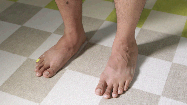 Un GIF fotográfico que muestra un primer plano de los pies de una persona que hace terneros se eleva sobre una alfombra a cuadros beige, tostado y verde lima.