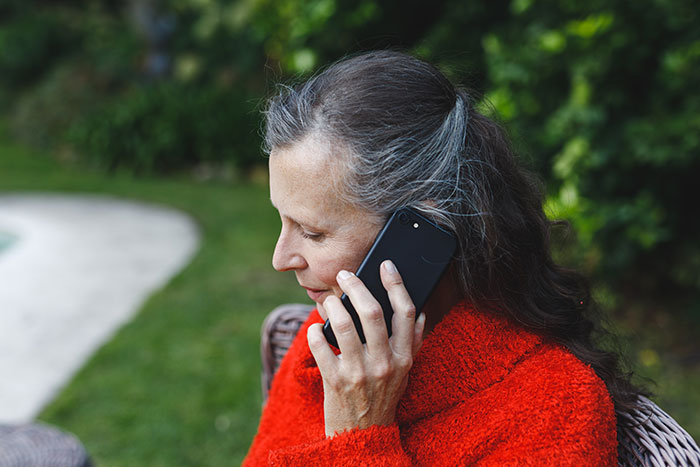 Mujer en suéter rojo al aire libre, hablando por teléfono, que representa al escenario de servicios de protección de suegra de suegra.