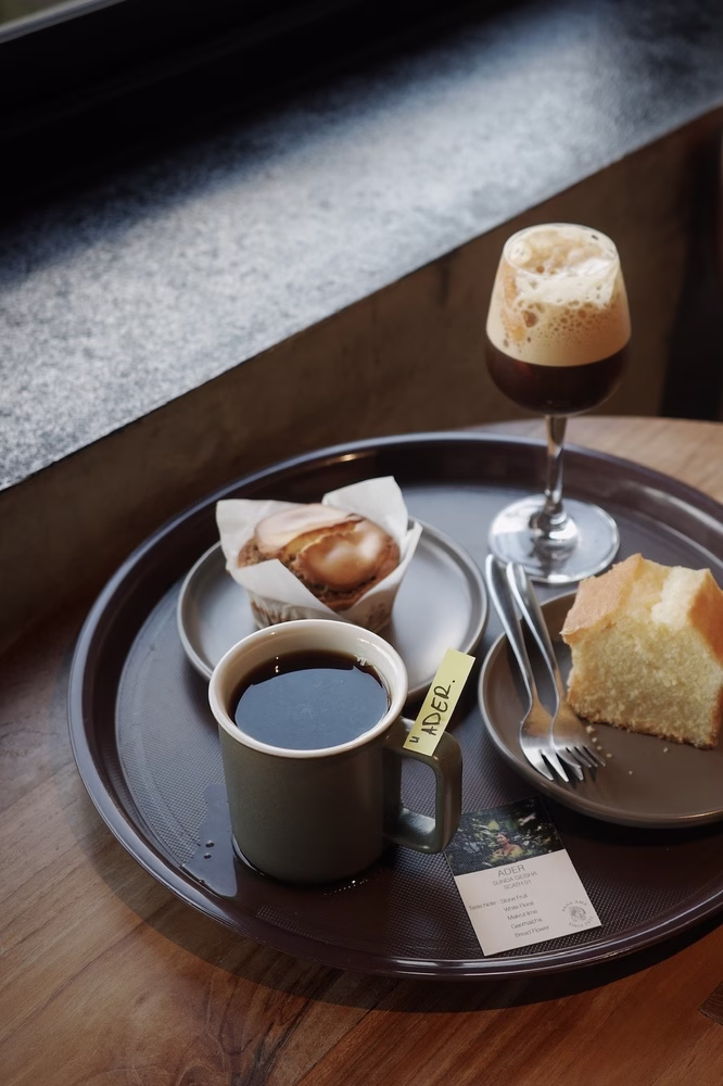 Hacia una industria más equitativa: en Akha Ama Coffee, una mesa de madera está cubierta con una bandeja llena de pasteles y una taza de café negro con una etiqueta que dice