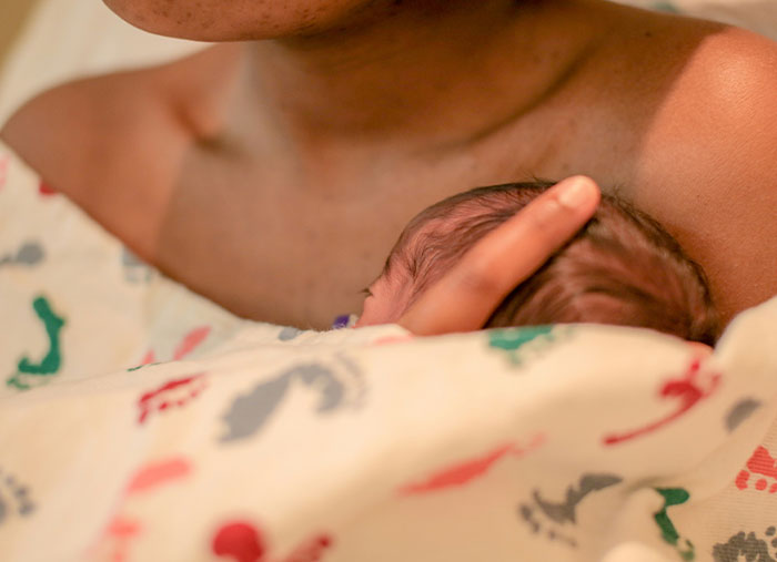 Nueva madre sosteniendo al recién nacido envuelto en una manta, mostrando un momento tierno relacionado con la UCIN y el cumplimiento malicioso.