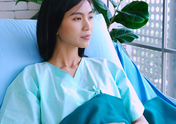 Nueva madre del vestido de hospital descansando junto a la ventana, reflejándose en silencio en un ambiente tranquilo de la UCIN.