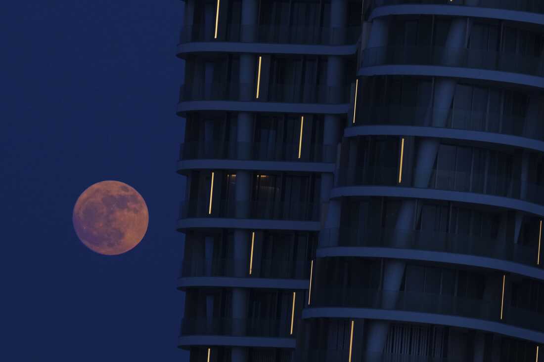 La luna de fresa se eleva detrás de una torre en un puerto deportivo