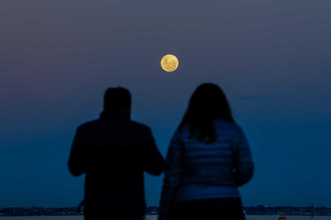 Una pareja mira la luna llena de fresa se eleva en Williamstown Beach