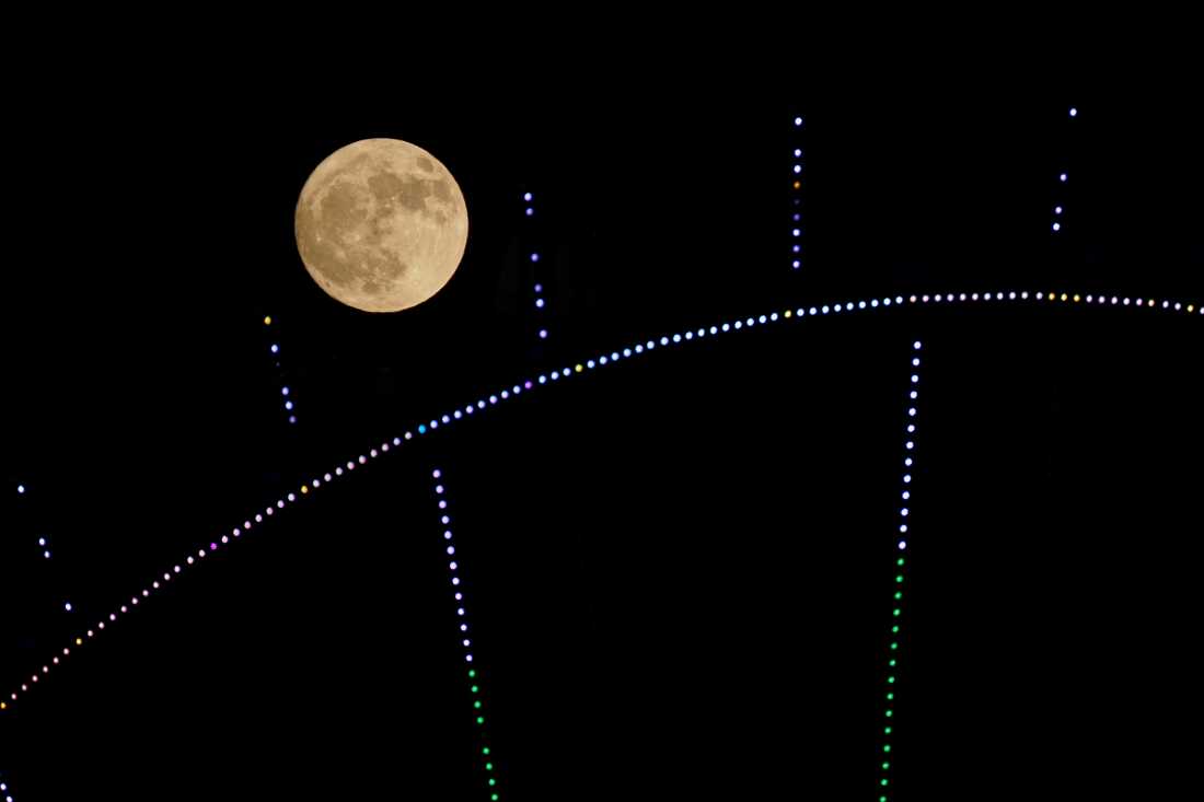 Se ve un gabinete de rueda de ferris frente a la luna llena
