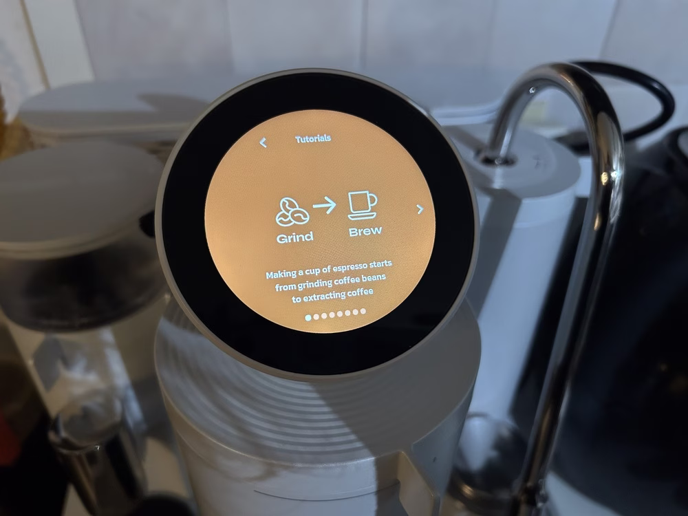 Una foto de la pantalla táctil en la máquina de café espresso casera de Meraki muestra un tutorial para principiantes sobre elaboración de café espresso, incluido el texto que describe que hacer una taza de espresso comienza con moler los granos de café.