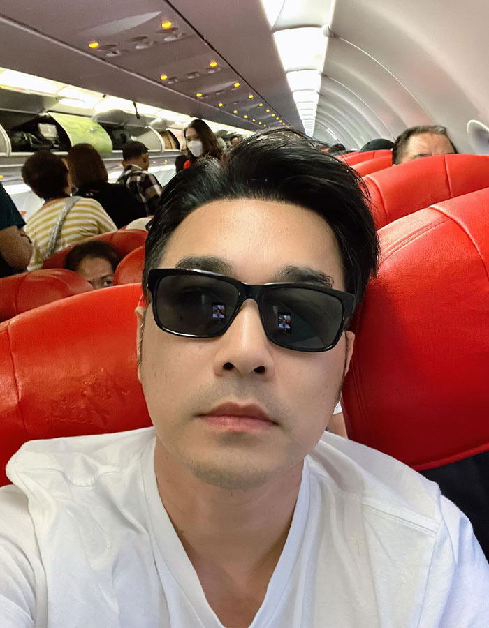 El actor tailandés con gafas de sol y camisa blanca, sentada en un avión, vinculado a la única historia de Survivor de accidentes aéreos de Air India.