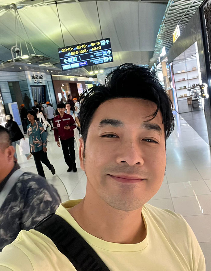 Actor tailandés sonriendo en el aeropuerto, destacando la supervivencia del accidente aéreo y el misterioso enlace a la única historia de sobrevivientes de Air India