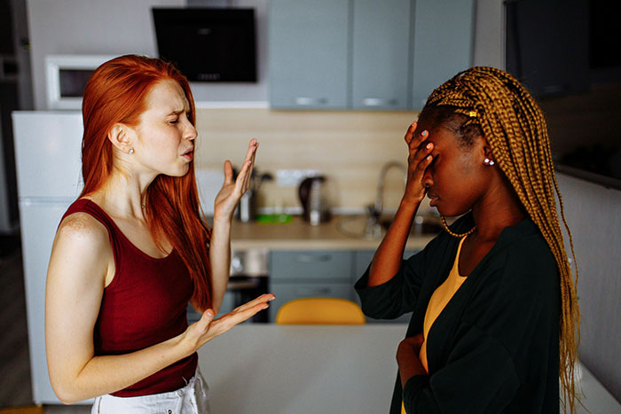 Dos mujeres en una cocina discutiendo intensamente, representando a una mujer que tiene suficiente prima insultando su boda y aplaudiendo.