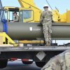 Los aviadores en uniformes de camuflaje miran una bomba GBU-57 en la Base de la Fuerza Aérea Whiteman en Missouri el 2 de mayo de 2023. La larga bomba cilíndrica verde oliva con extremo puntiagudo se encuentra horizontal en una cama de camión.