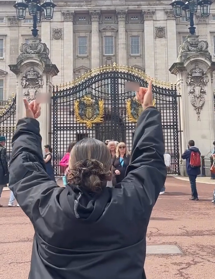 Persona con dedos medios elevados frente a las puertas del Palacio de Buckingham, vinculada al debate sobre el cuello del artista aborigen del artista aborigen.