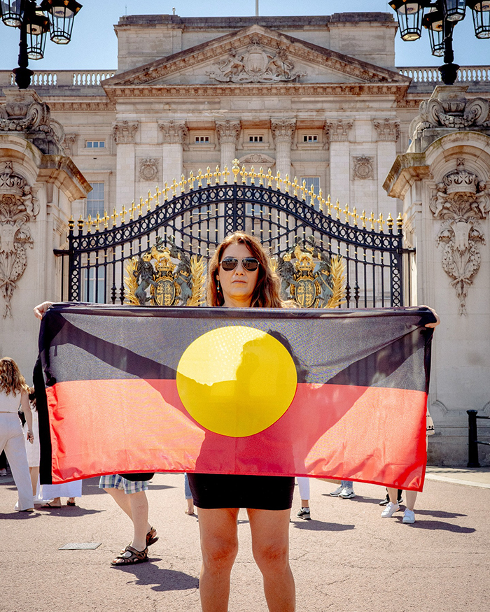 Artista aborigen sosteniendo la bandera fuera del Palacio de Buckingham, provocando un debate relacionado con la controversia del Rey Charles.