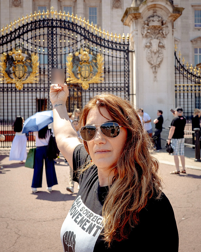 Artista aborigen con gafas de sol y levantando un puño frente a las puertas del palacio de Buckingham durante una protesta.