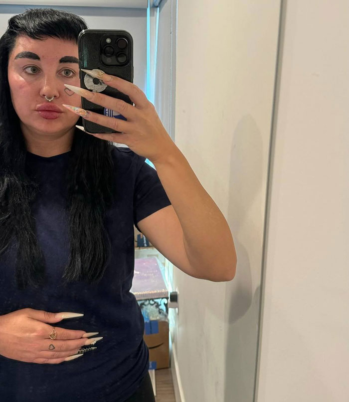 Amanda Bynes tomando una selfie de espejo en el interior, mostrando uñas largas y vistiendo una camisa azul marino después de revelar el uso de Ozempic.