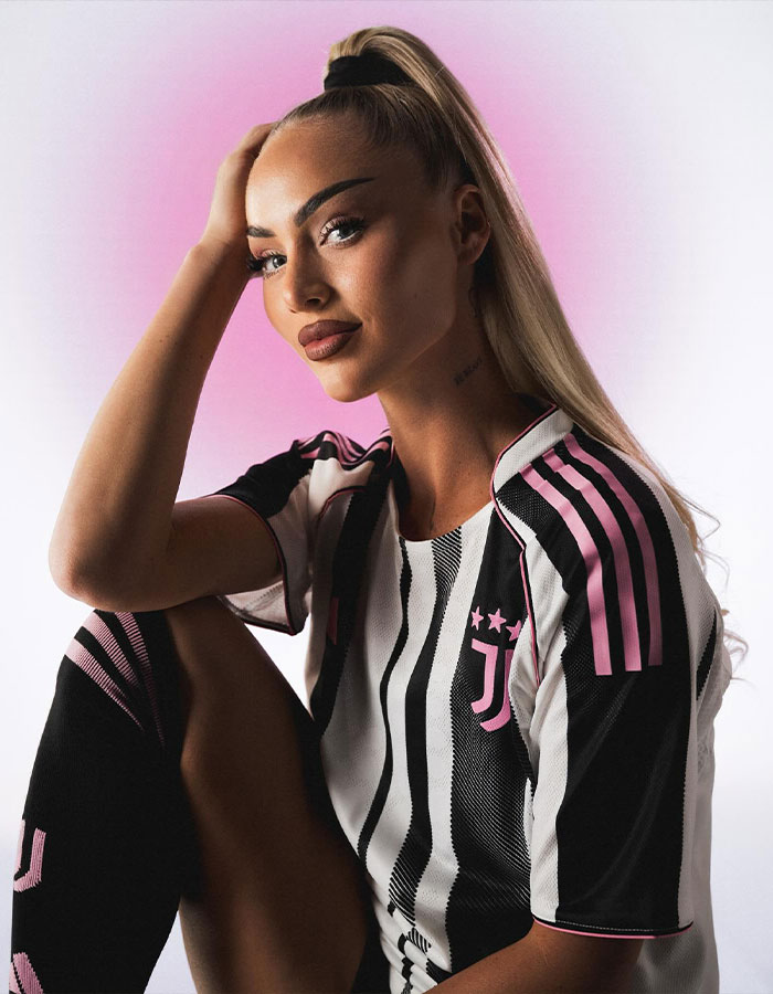 Jugador de equipo nacional de fútbol femenino posando en jersey a rayas en blanco y negro con acentos rosados ​​contra un fondo rosa suave.