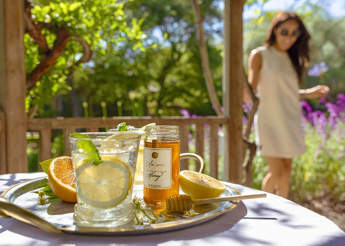 Bandeja con frasco de miel, limón, naranja y un vaso de agua de limón al aire libre, relacionado con la controversia de productos de la marca Meghan Markle.