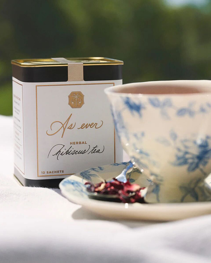 Como siempre la caja de té de hibisco herbal con una taza de té floral azul y un platillo sobre un fondo de tela blanca.