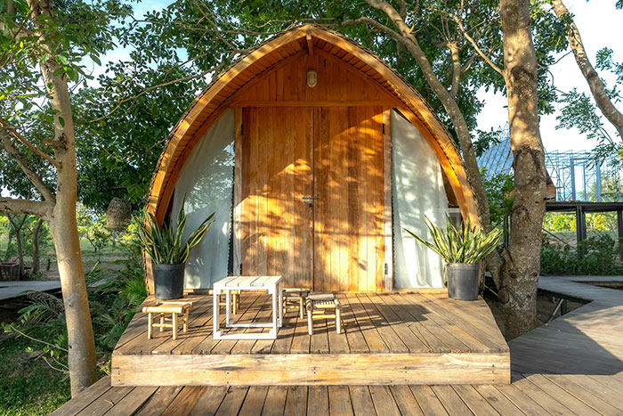 La acogedora cabaña de madera rodeada de árboles con un pequeño porche y un asiento al aire libre que atrae a inquilinos y vecinos.