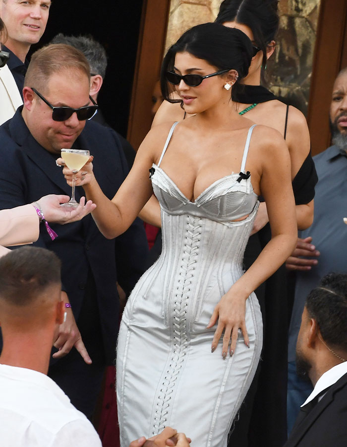 Kylie Jenner con un vestido de corsé y gafas de sol en la celebración de la boda de Lauren Sánchez, sosteniendo un vaso de cóctel.