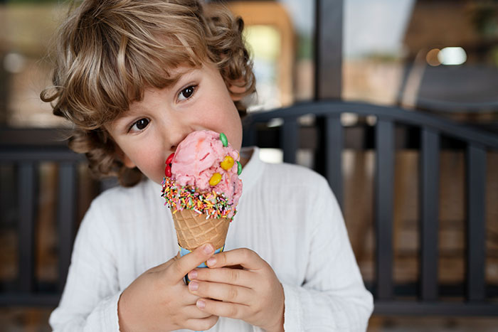 Niño pequeño que come colorido cono de helado, que ilustra a los parientes boomer que socavan los hábitos saludables de los niños con dulces y refrescos.