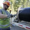 En esta foto de archivo 2021, un trabajador del distrito de servicios públicos del condado de Mason en el estado de Washington instala una percha en el cable de fibra óptica a medida que sale de un carrete.