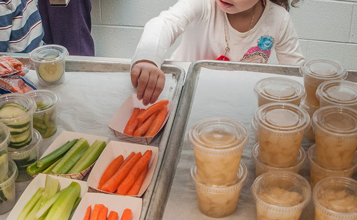 Niño que buscan zanahorias en una bandeja con almuerzos escolares estadounidenses con verduras y tazas de frutas en un entorno de cafetería