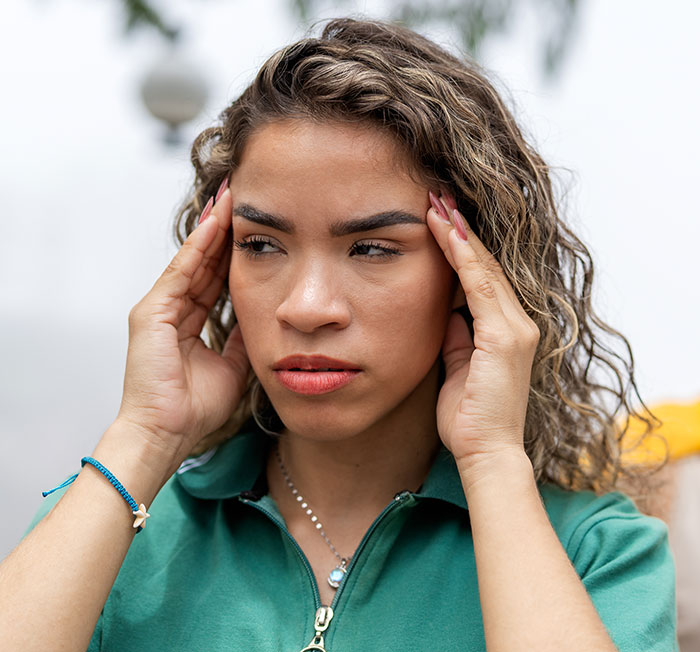 Mujer con cabello rizado que se ve estresada y preocupada, sosteniendo sus sienes, relacionadas con el conflicto de servicios de protección infantil.