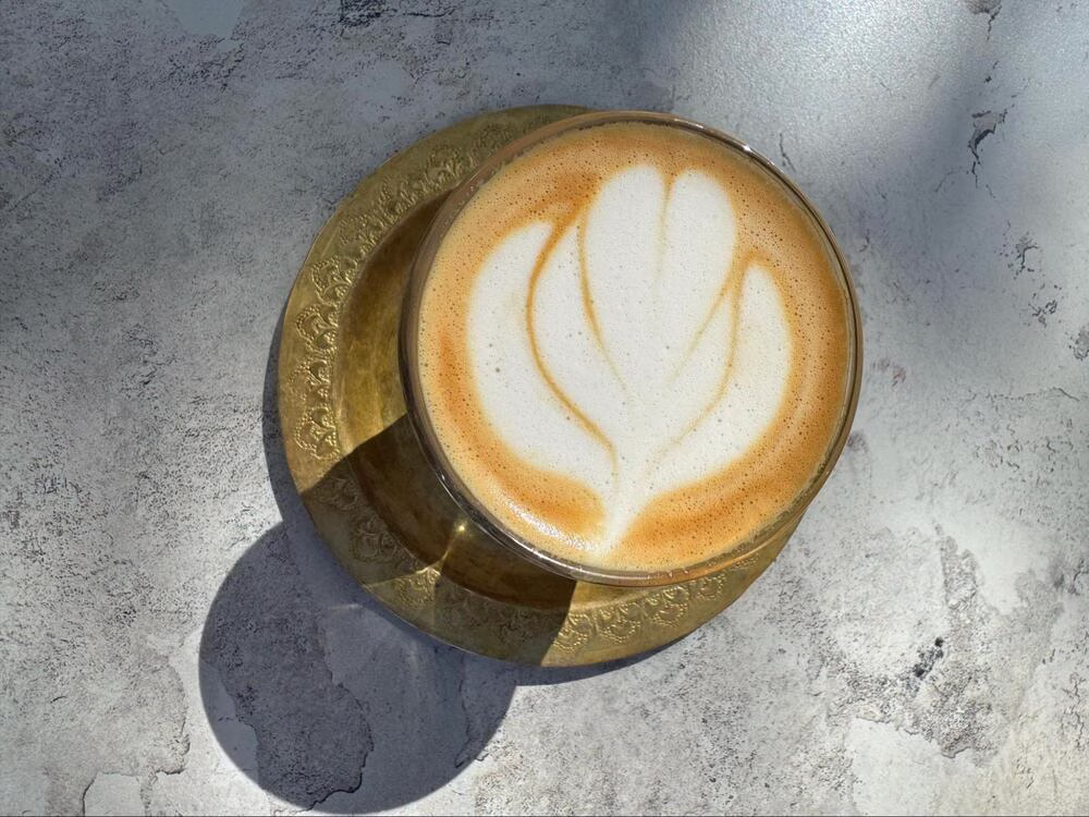 Una imagen superior de un Cortado con arte de leche con forma de corazón. El Cortado se sienta en un platillo dorado.