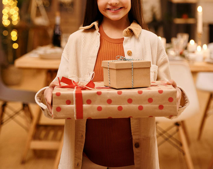 Young Girl sosteniendo regalos de cumpleaños envueltos, simbolizando el tema del niño dorado en un entorno cálido interior.
