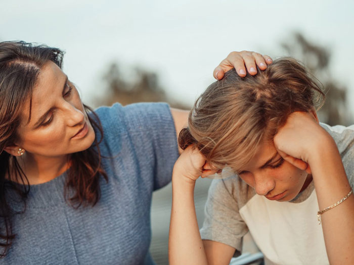Mujer reconfortante molesto adolescente al aire libre, ilustrando un conflicto infantil dorado que involucra regalos robados y tensión entre hermanos.