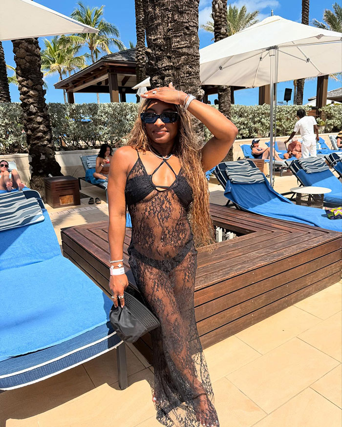 Simone Biles con un encubrimiento de traje de baño de encaje negro, con gafas de sol y un brazalete, posando junto a la piscina durante unas vacaciones soleadas.