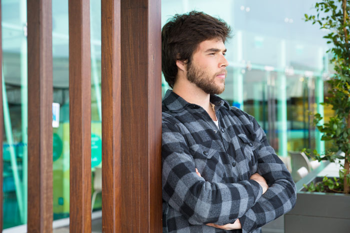 El joven en camisa a cuadros apoyada contra la pared de madera, reflexionando sobre la amistad y la referencia de empleo después del divorcio.