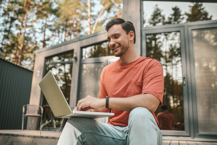 Hombre que usa la computadora portátil al aire libre, sonriendo a medida que escribe, representando a un tipo que busca la referencia de trabajo después del divorcio y el amigo fantasma.