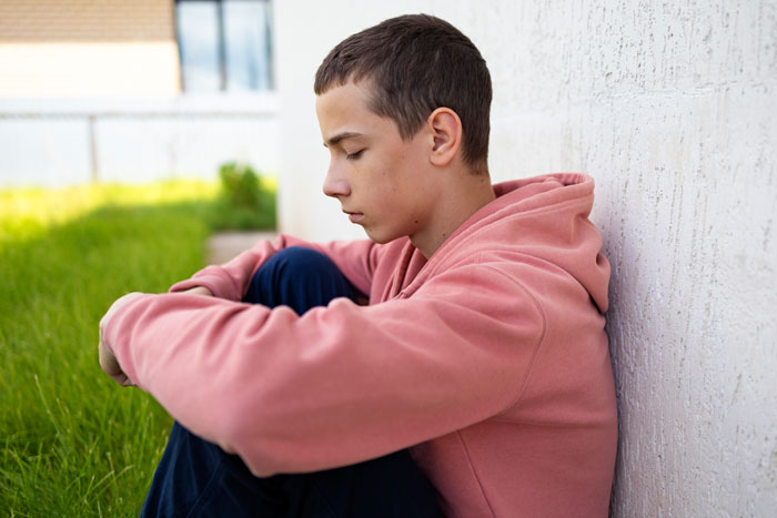 Teen Boy In Pink Soodie Situe sola afuera, pareciendo molestos por los padres que ignoran su cumpleaños y las alergias de su hermanastras.