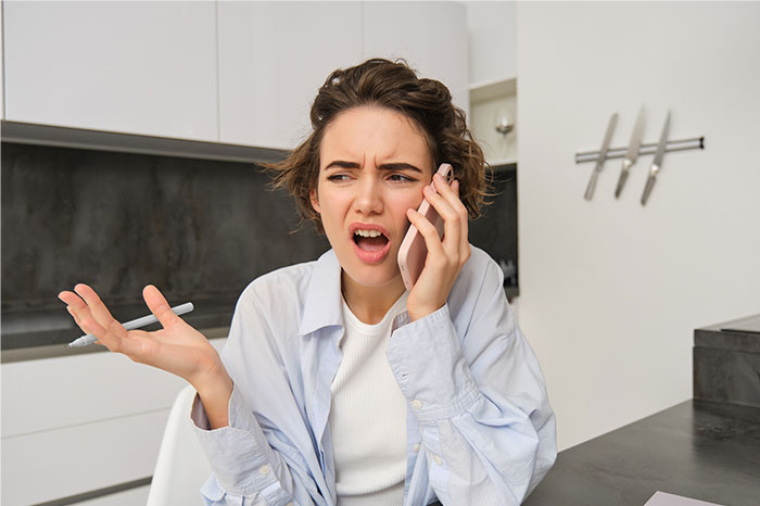 Mujer joven que parece frustrada mientras habla por teléfono, expresando derecho sobre el pago de alquiler de la nuera.