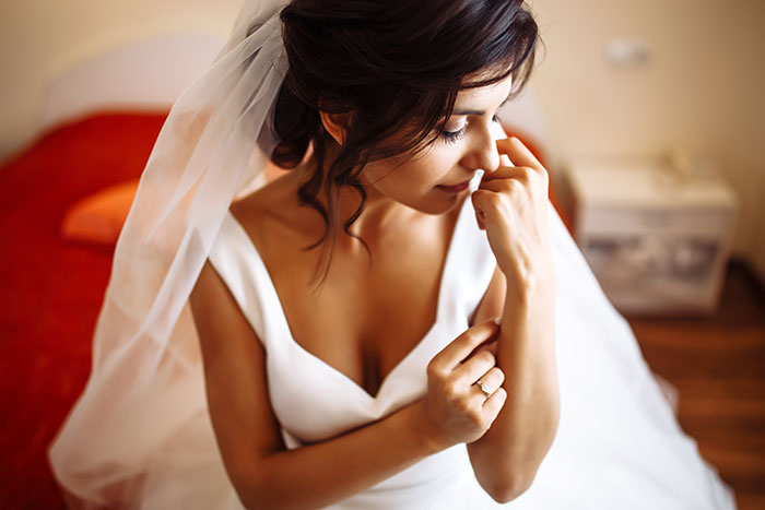 Novia con vestido blanco y velo sentado en el interior, reflexionando en la ocasión con una expresión suave y reflexiva.