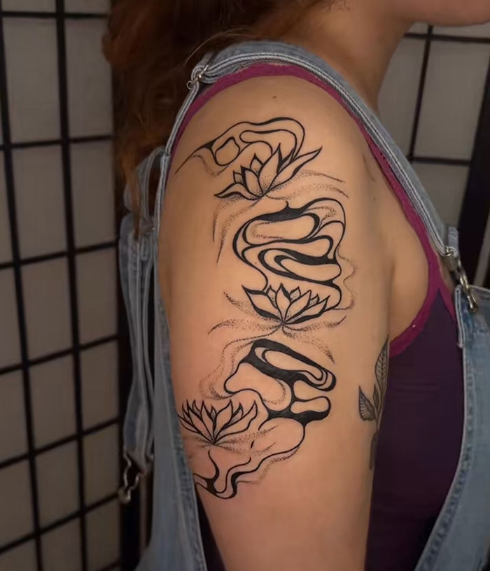 Abstracto de tatuaje de flores de loto negro en la parte superior del brazo de una mujer por un artista de tatuajes que se vuelve viral en línea.