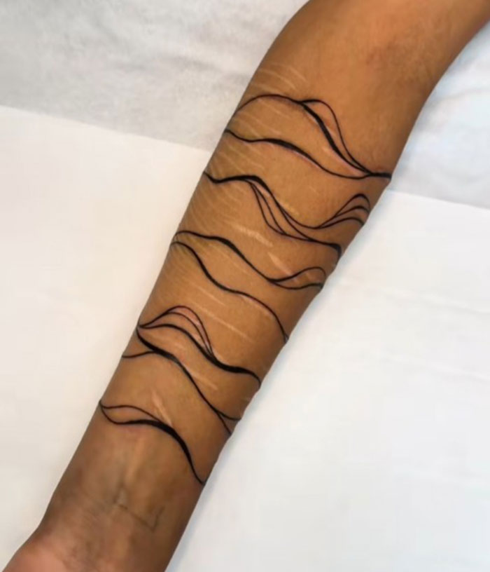 Primer plano de un brazo que muestra los encubrimientos de un artista de tatuajes con líneas abstractas en forma de ola negra que ocultan las marcas antiguas.
