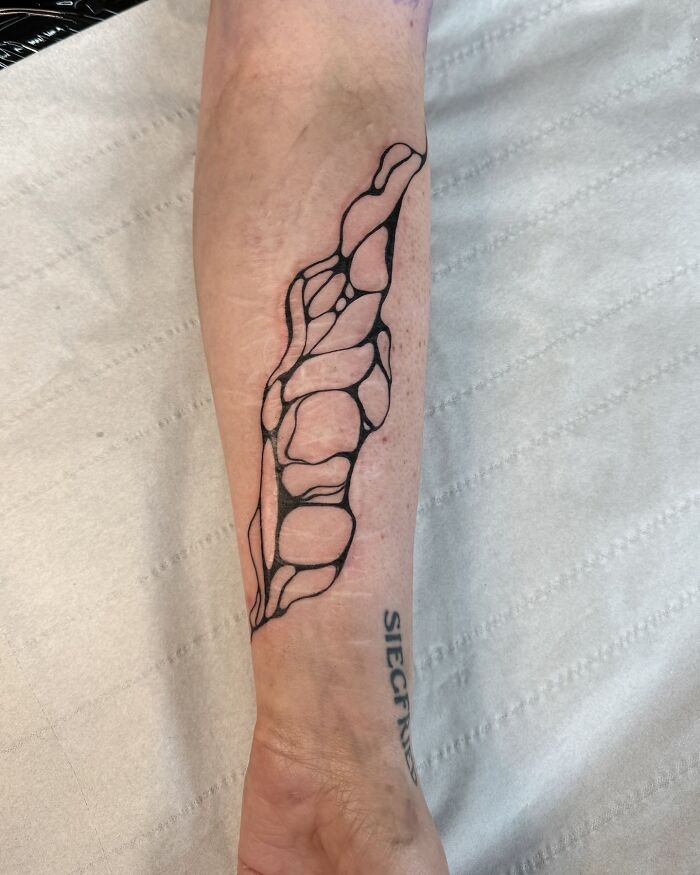 Abstracto de tatuaje de tatuaje de línea negra en el antebrazo interno por artista de tatuajes, mostrando encubrimientos creativos virales.