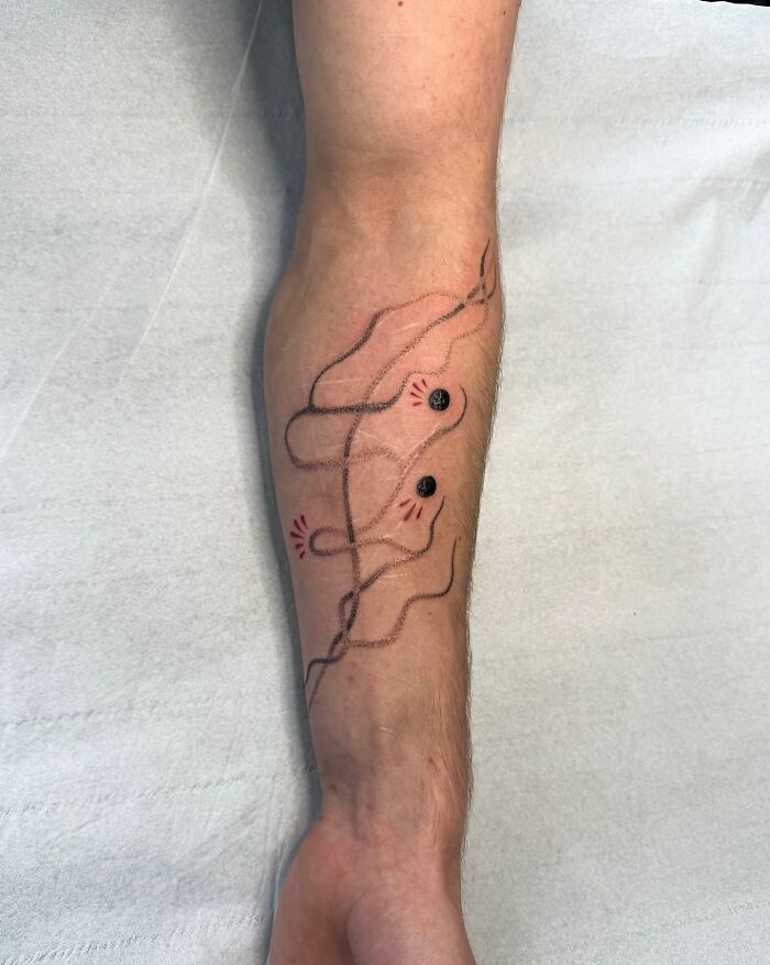 Resumen de tatuaje mínimo de tatuaje en un antebrazo con líneas finas y pequeños acentos rojos por un artista de tatuajes.
