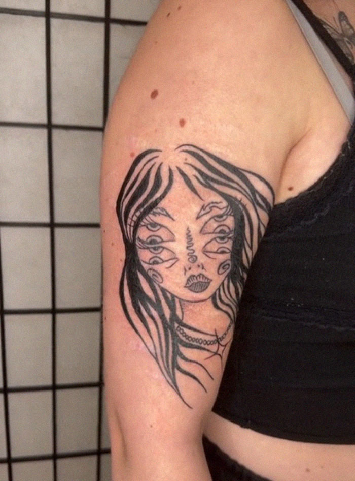 Abstracto de tatuaje de tinta negra en la parte superior del brazo que muestra a una mujer surrealista con múltiples ojos del artista de tatuajes.