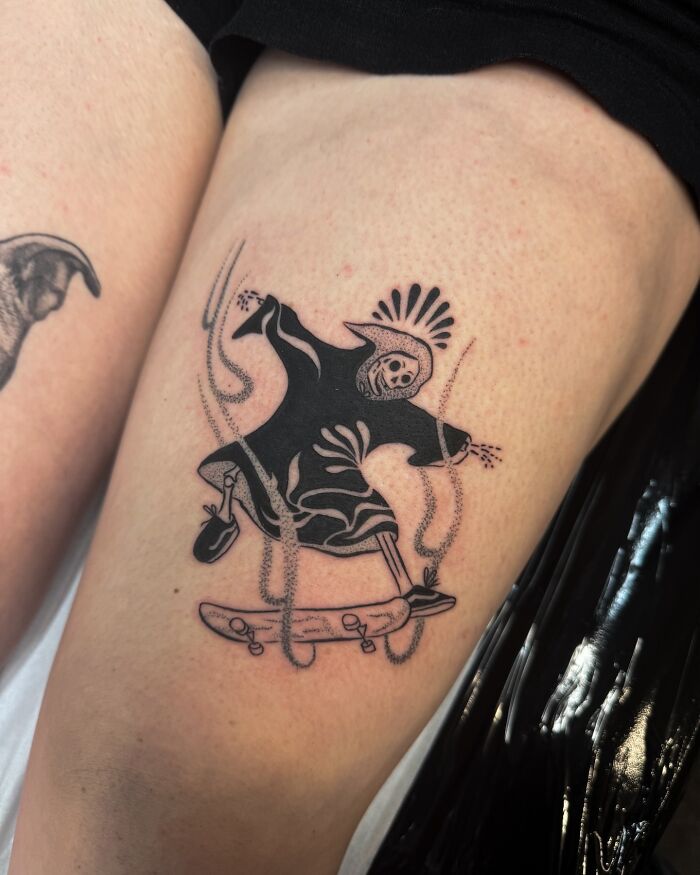 Tatuaje de tatuaje de tatuaje de un skate de esqueleto, diseño detallado de tinta negra en la parte superior del muslo de una persona.