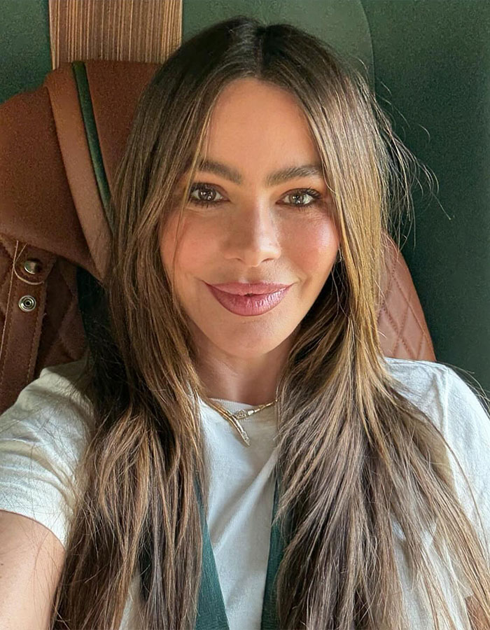 Sofía Vergara sonriendo con cabello largo y maquillaje natural en un entorno informal, mostrando su belleza y encanto sin esfuerzo.